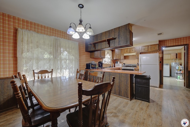 dining room featuring washer / dryer, light wood finished floors, wallpapered walls, and an inviting chandelier