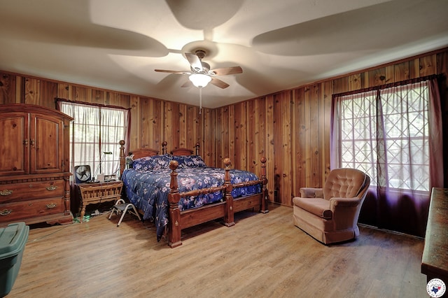 bedroom with light wood-style floors, wood walls, a ceiling fan, and multiple windows