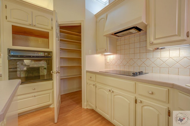 kitchen with light hardwood / wood-style floors, black appliances, cream cabinetry, and custom exhaust hood