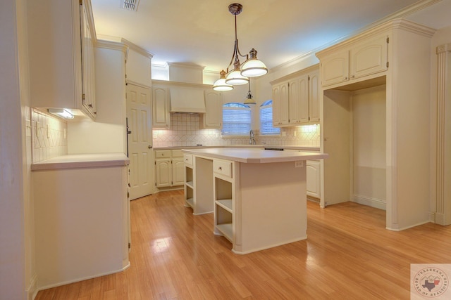 kitchen with light hardwood / wood-style floors, premium range hood, sink, a kitchen island, and pendant lighting