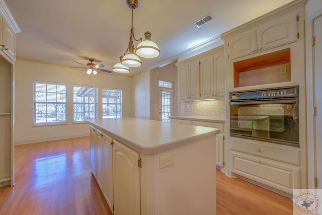 kitchen with a kitchen island, oven, hanging light fixtures, and ornamental molding