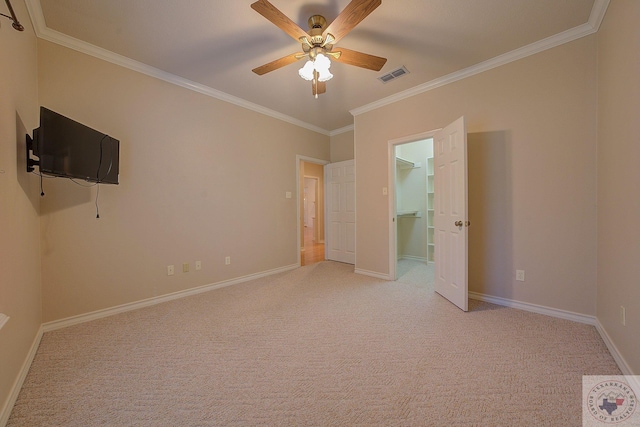 unfurnished bedroom with ceiling fan, crown molding, light carpet, and a walk in closet