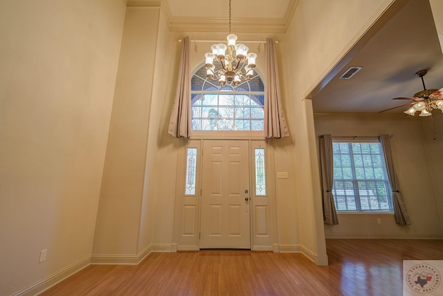 foyer with ceiling fan with notable chandelier, plenty of natural light, crown molding, and light wood-type flooring