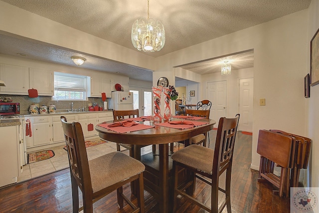 dining space featuring french doors, sink, a textured ceiling, dark hardwood / wood-style floors, and an inviting chandelier