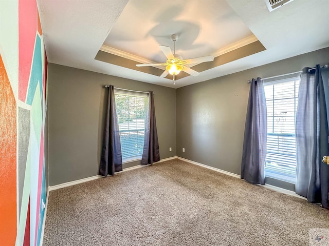 carpeted empty room featuring ceiling fan, plenty of natural light, and a tray ceiling