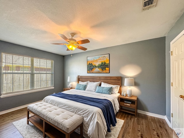 bedroom with ceiling fan, a textured ceiling, and dark hardwood / wood-style flooring