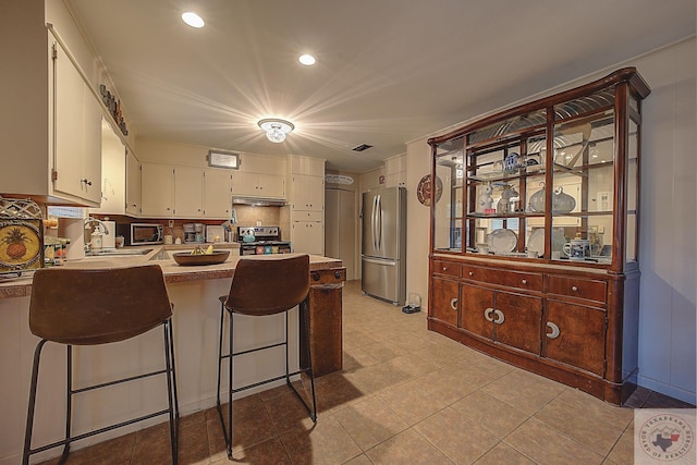 kitchen with kitchen peninsula, appliances with stainless steel finishes, sink, white cabinetry, and light tile patterned flooring