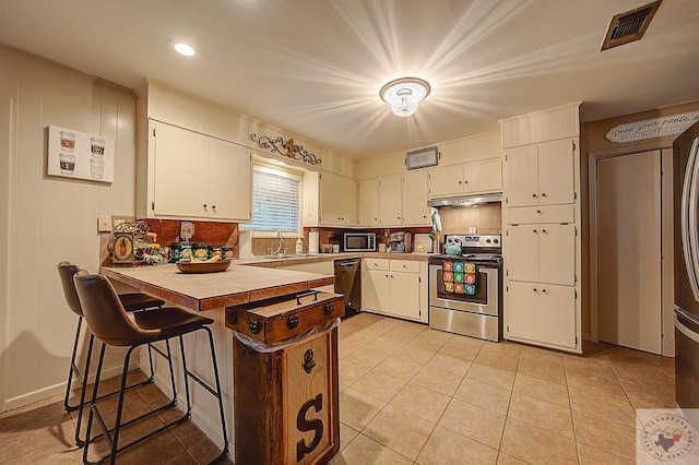 kitchen featuring built in microwave, white cabinets, stainless steel range with electric cooktop, light tile patterned flooring, and a kitchen bar