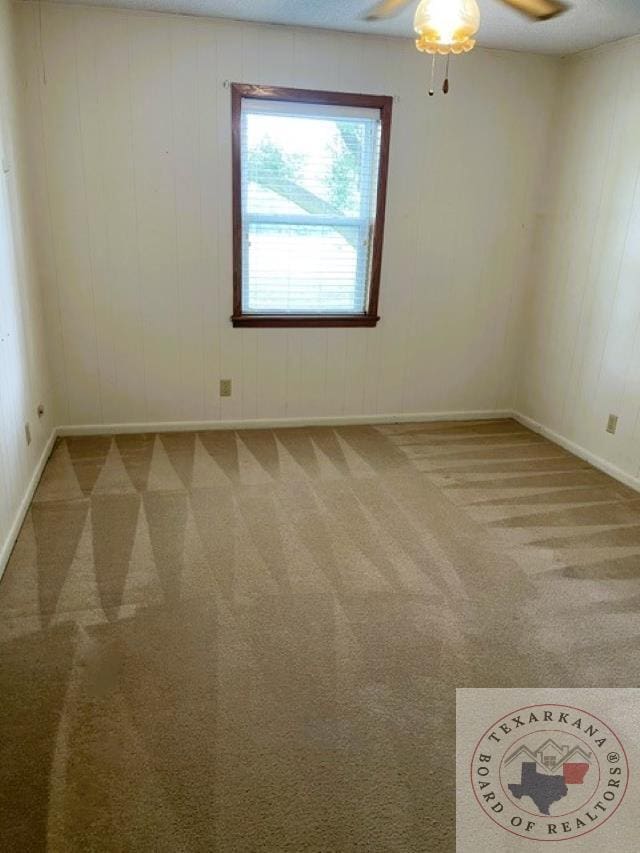 carpeted spare room featuring ceiling fan and wooden walls