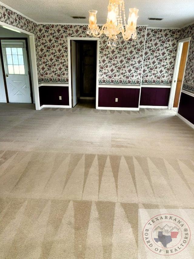 carpeted spare room with a textured ceiling and a chandelier