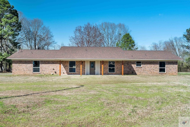 rear view of house with a shingled roof, brick siding, and a lawn