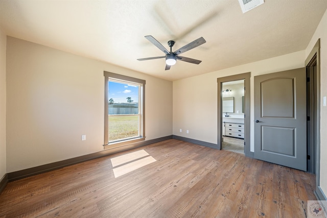 unfurnished bedroom with baseboards, visible vents, ceiling fan, wood finished floors, and ensuite bathroom