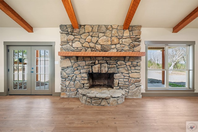 unfurnished living room featuring baseboards, french doors, wood finished floors, beamed ceiling, and a stone fireplace