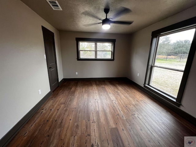 unfurnished room featuring ceiling fan, plenty of natural light, a textured ceiling, and dark hardwood / wood-style flooring