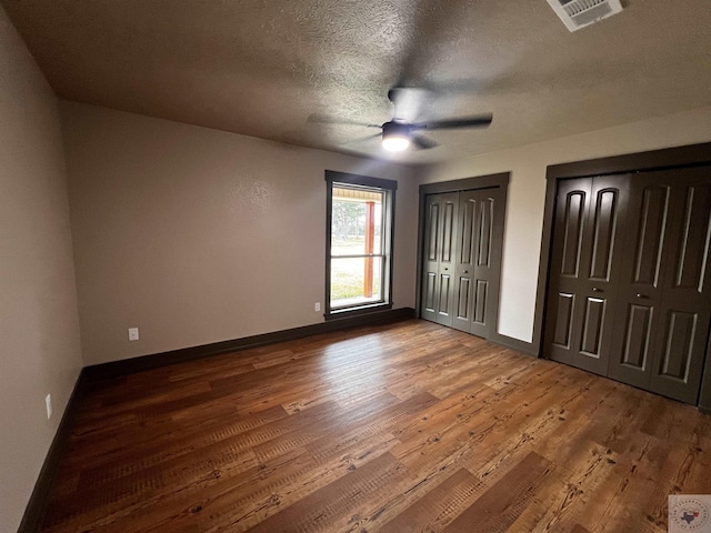 unfurnished bedroom with multiple closets, hardwood / wood-style flooring, a textured ceiling, and ceiling fan