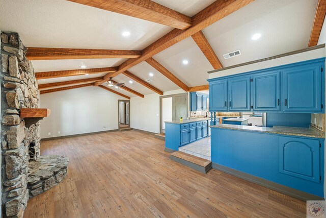 kitchen featuring vaulted ceiling with beams, a stone fireplace, blue cabinets, a peninsula, and visible vents