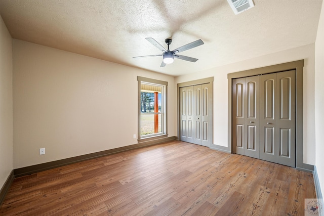 unfurnished bedroom featuring baseboards, visible vents, wood finished floors, a textured ceiling, and multiple closets