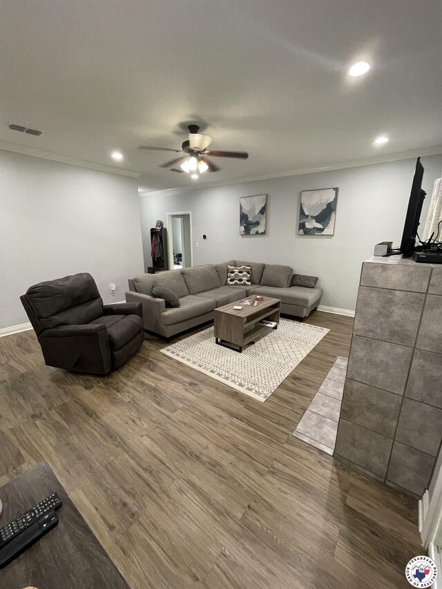living room featuring a ceiling fan, visible vents, ornamental molding, and dark wood-style flooring