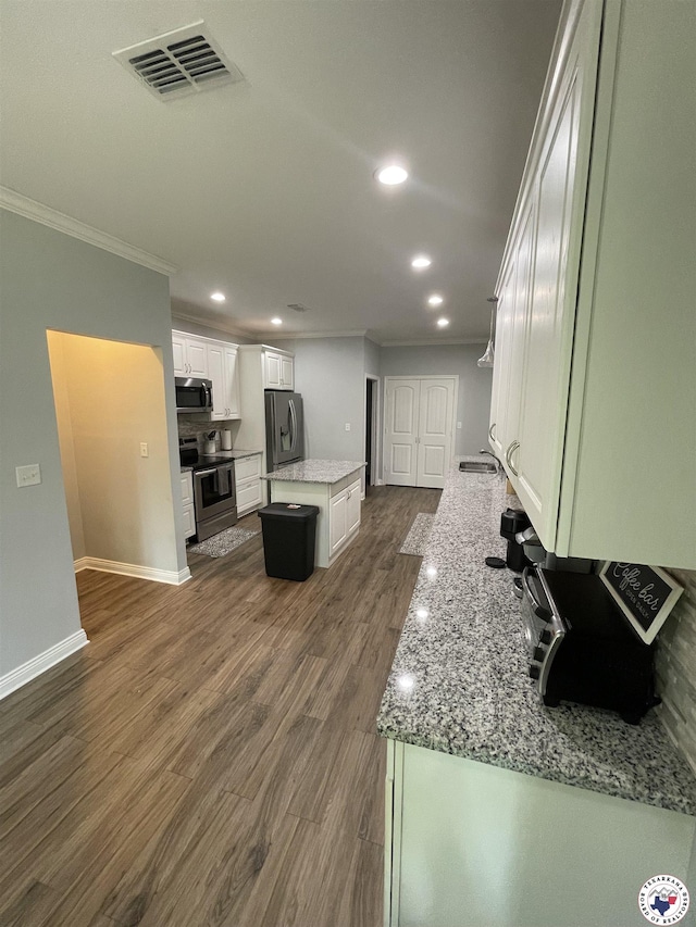 kitchen with white cabinets, visible vents, ornamental molding, a kitchen island, and appliances with stainless steel finishes