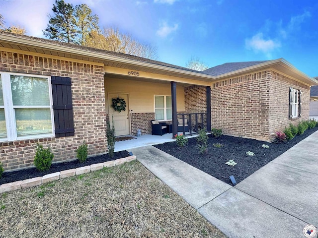 view of exterior entry featuring brick siding and covered porch