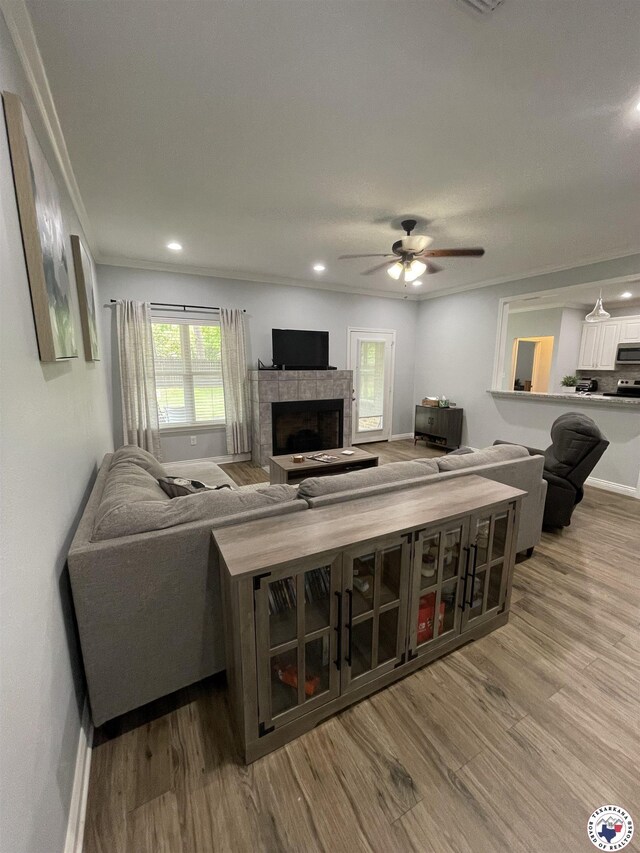living area featuring wood finished floors, crown molding, baseboards, a tiled fireplace, and ceiling fan