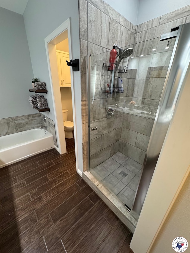 bathroom with a garden tub, toilet, wood finished floors, and a stall shower