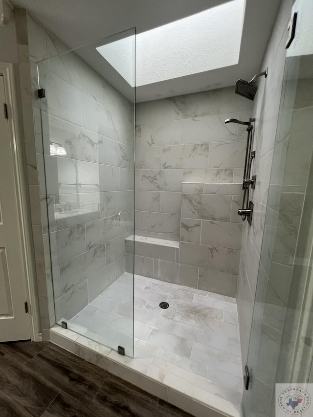 bathroom featuring wood-type flooring, tiled shower, and a skylight