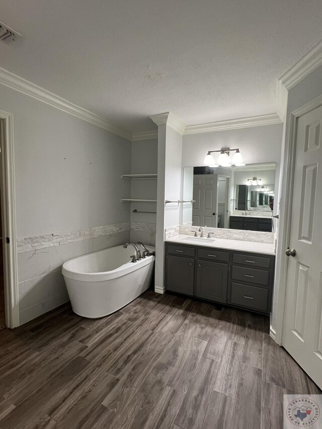 bathroom with crown molding, wood-type flooring, a tub, a textured ceiling, and vanity