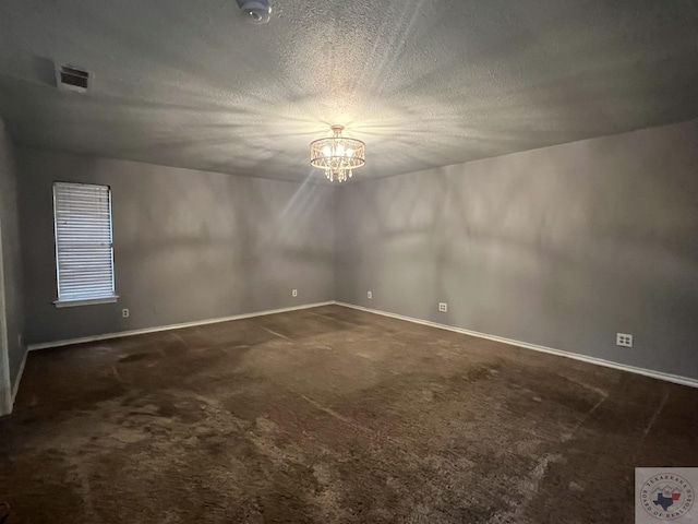 empty room featuring a notable chandelier, dark carpet, and a textured ceiling