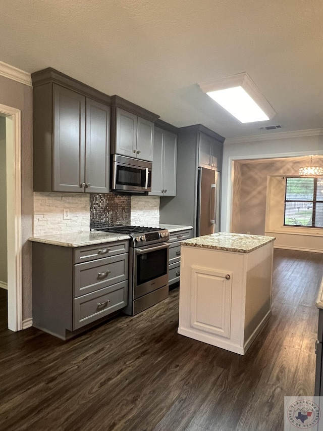 kitchen with appliances with stainless steel finishes, a kitchen island, dark hardwood / wood-style flooring, gray cabinetry, and crown molding