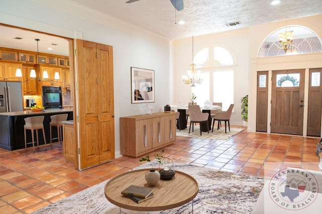 entryway with ceiling fan with notable chandelier, crown molding, light tile patterned floors, and a textured ceiling