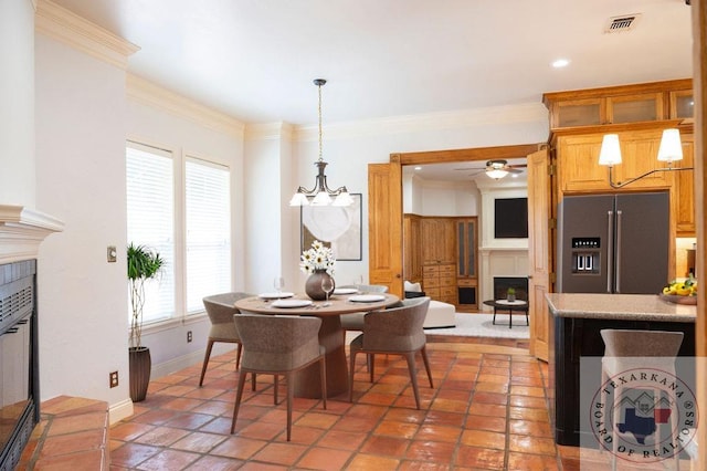 tiled dining space featuring ceiling fan with notable chandelier, a tile fireplace, and crown molding