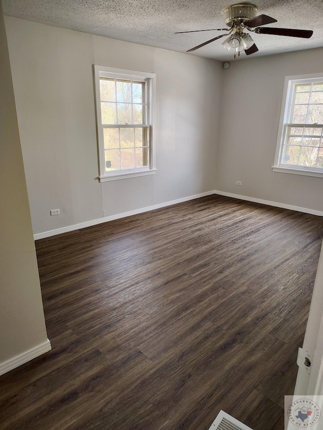 empty room with ceiling fan, dark wood-type flooring, a textured ceiling, and a healthy amount of sunlight