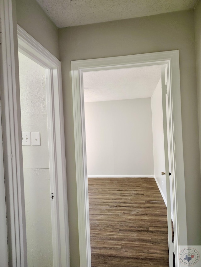 hall featuring a textured ceiling, baseboards, and dark wood-type flooring