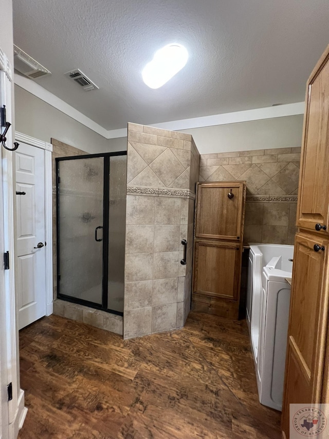 bathroom featuring wood-type flooring, independent shower and bath, tile walls, independent washer and dryer, and a textured ceiling