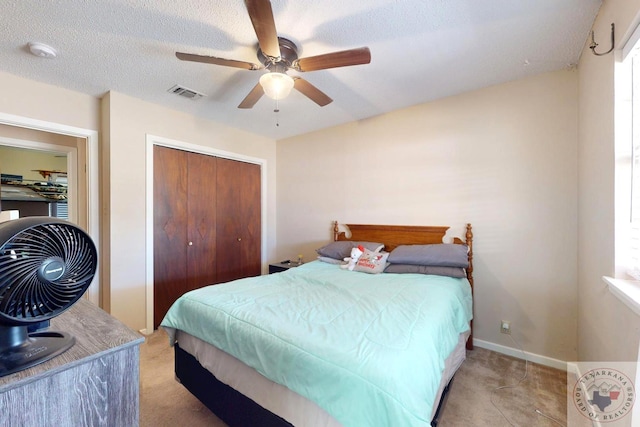 bedroom with a closet, light colored carpet, visible vents, a ceiling fan, and a textured ceiling