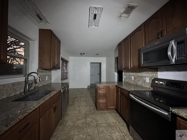 kitchen with sink, stainless steel appliances, kitchen peninsula, and dark stone counters