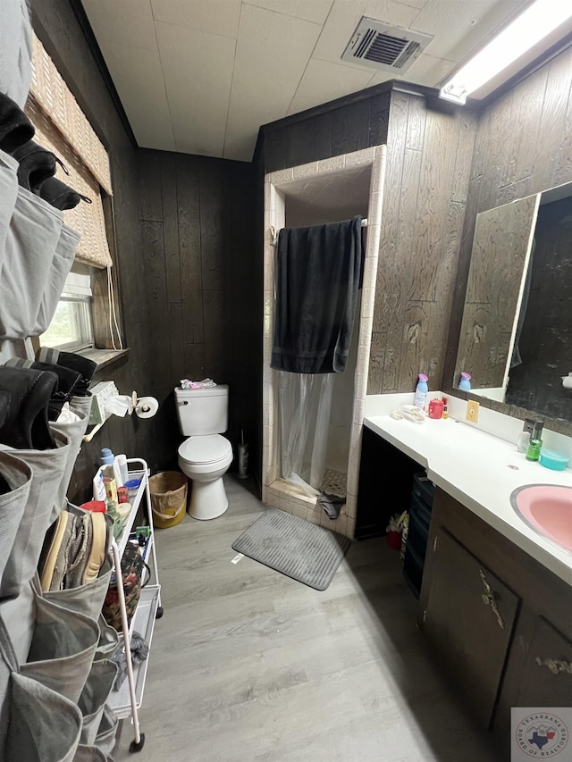 bathroom with toilet, wood-type flooring, walk in shower, vanity, and wood walls