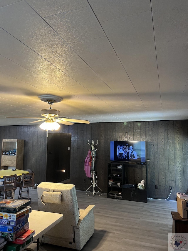 living room featuring ceiling fan, hardwood / wood-style flooring, and wood walls