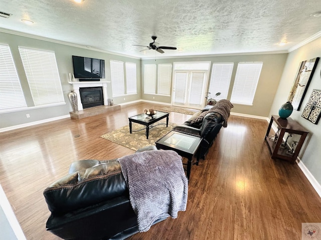 living room featuring wood-type flooring, a textured ceiling, ceiling fan, and ornamental molding