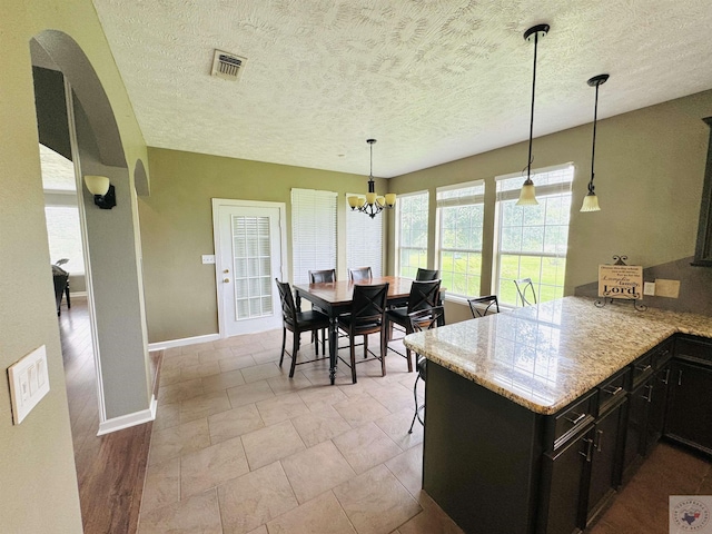 kitchen with light stone countertops, pendant lighting, an inviting chandelier, kitchen peninsula, and light tile patterned floors