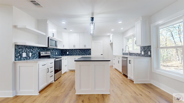 kitchen with light wood-type flooring, white cabinetry, hanging light fixtures, and appliances with stainless steel finishes