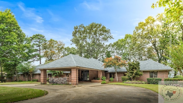 view of front of house with roof with shingles, a front yard, concrete driveway, and brick siding