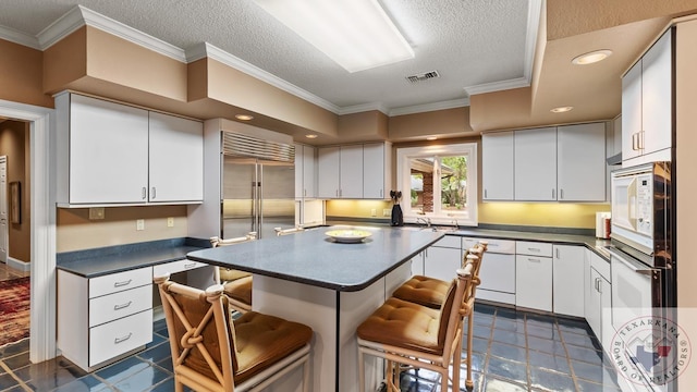 kitchen featuring dark tile patterned floors, white cabinets, white appliances, a kitchen bar, and a textured ceiling