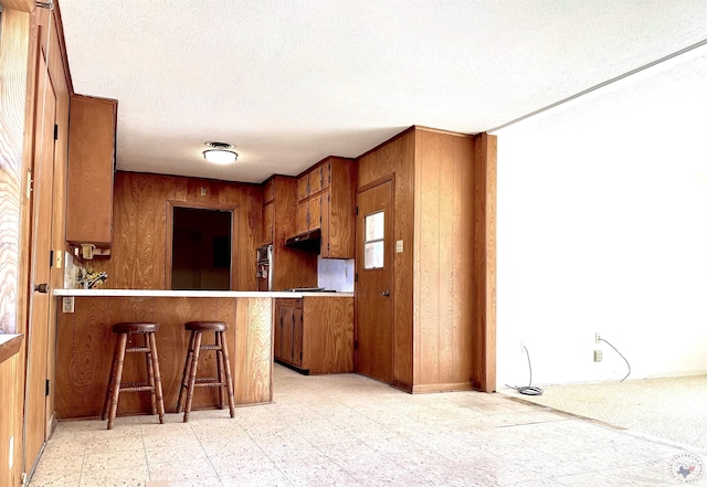 129 Pine St, Maud, TX 75567 - kitchen with wood walls, light floors, stainless steel oven, a kitchen bar, and brown cabinets