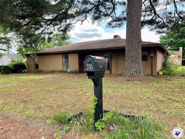 single story home featuring a chimney, brick siding, and a front yard