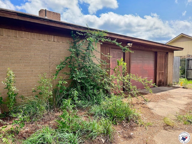 view of home's exterior featuring a chimney, brick siding, fence, driveway, and an attached garage