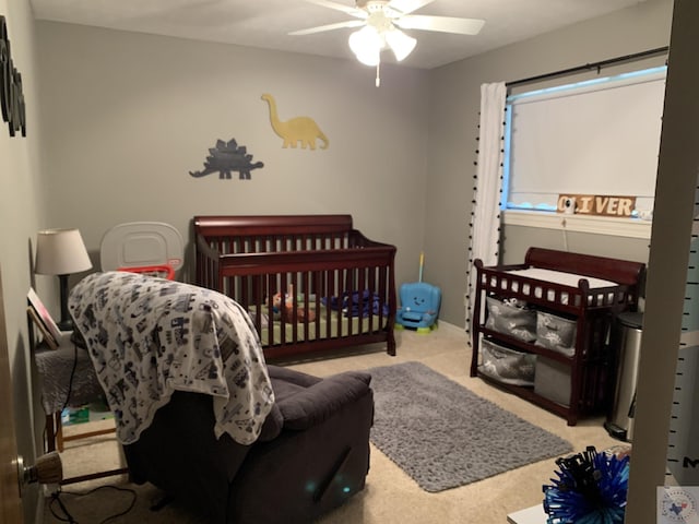 carpeted bedroom with ceiling fan and a crib