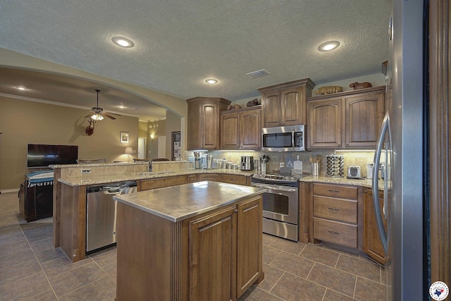 kitchen with visible vents, a peninsula, a kitchen island, a ceiling fan, and appliances with stainless steel finishes