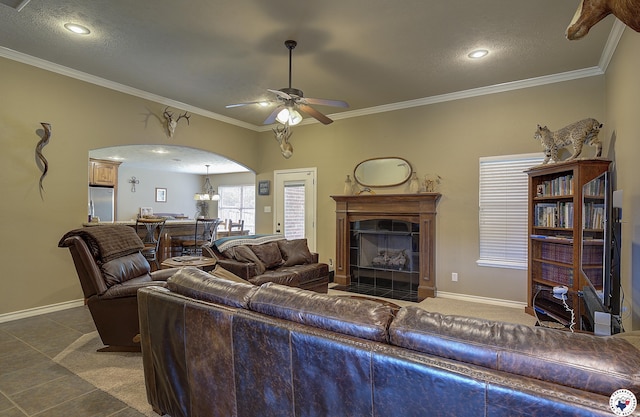 living area featuring a ceiling fan, crown molding, arched walkways, a fireplace, and baseboards